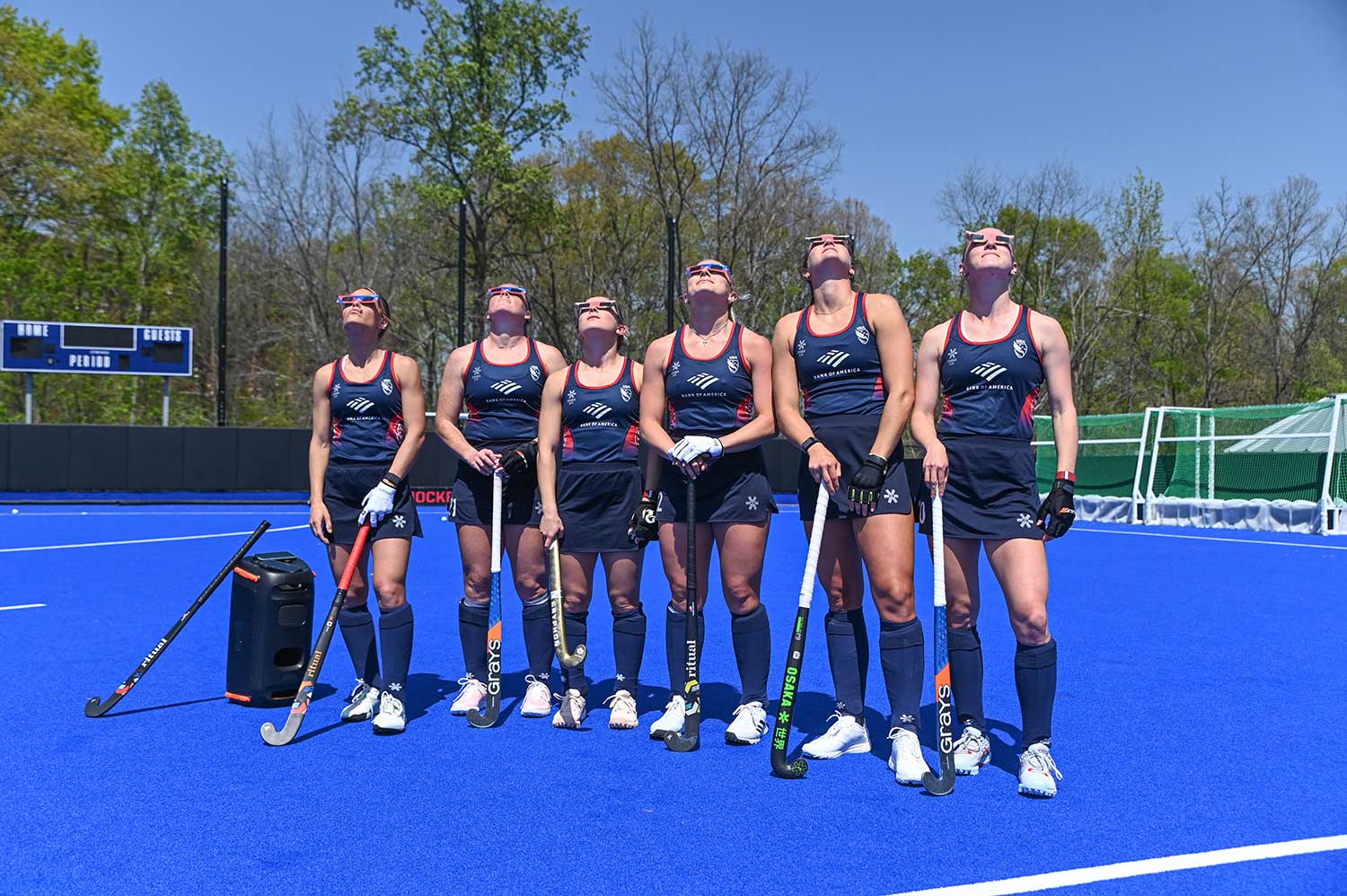 Six field hockey players standing on the field looking up at the sky.