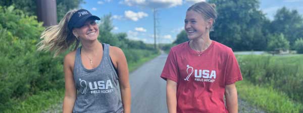 Two smiling girls wearing USA field hockey apparel.