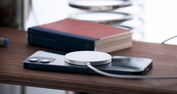 iPhone avec un chargeur MagSafe posé sur un bureau en bois avec un livre en arrière plan