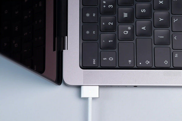 MacBook vue de haut avec un chargeur MagSafe pour Mac branché sur fond gris