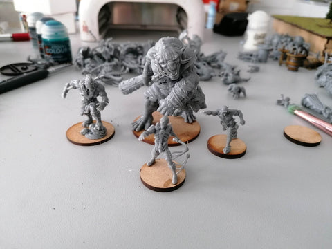 A cursed Empire Trogre miniature surrounded by 3 Cursed Empire Darkuns and with a pile of printed miniatures in the background with a UV curing device