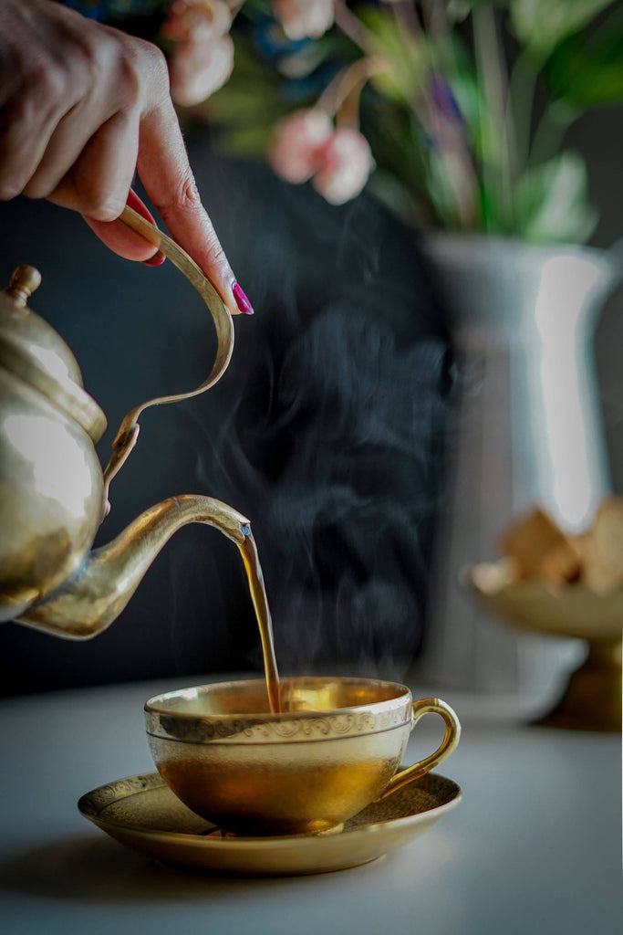 person pouring tea on gold ceramic teapot