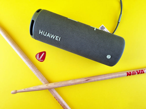 Una púa de guitarra, baquetas y un altavoz portátil Huawei sobre una superficie amarilla