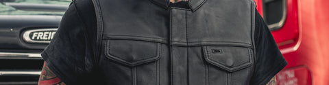 Man wearing solid black leather motorcycle vest with double chest pockets low banded collar front zipper with covered snaps solid back