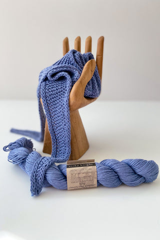 Blue hand knitted neckerchief resting on wooden hand with skein of studio linen by Erika knight sitting alongside