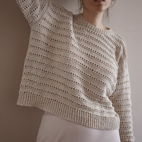 Woman standing in boxy cream knitted summer sweater with decorative eyelet details