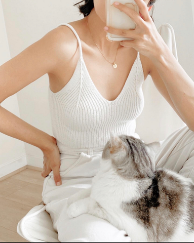 Woman wearing knitted white camisole with a cat on her lamp