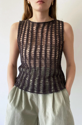 Woman standing wearing open weave knitted singlet with hands in trouser pockets