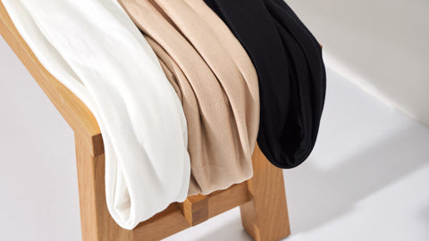 White, beige and black knit fabrics hanging over wooden bench against white backdrop