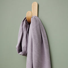 Close up of light purple coloured sewing fabric hanging over wooden wall hook on green background