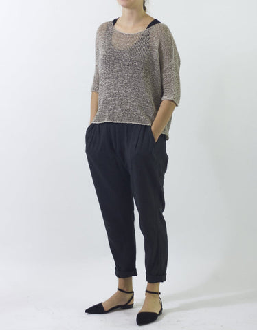 Woman standing in sheer, grey knitted sweater with hands in pockets