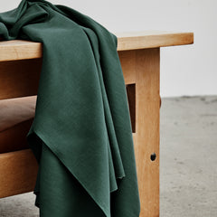 Dark green woven sewing fabric draped over wooden bench