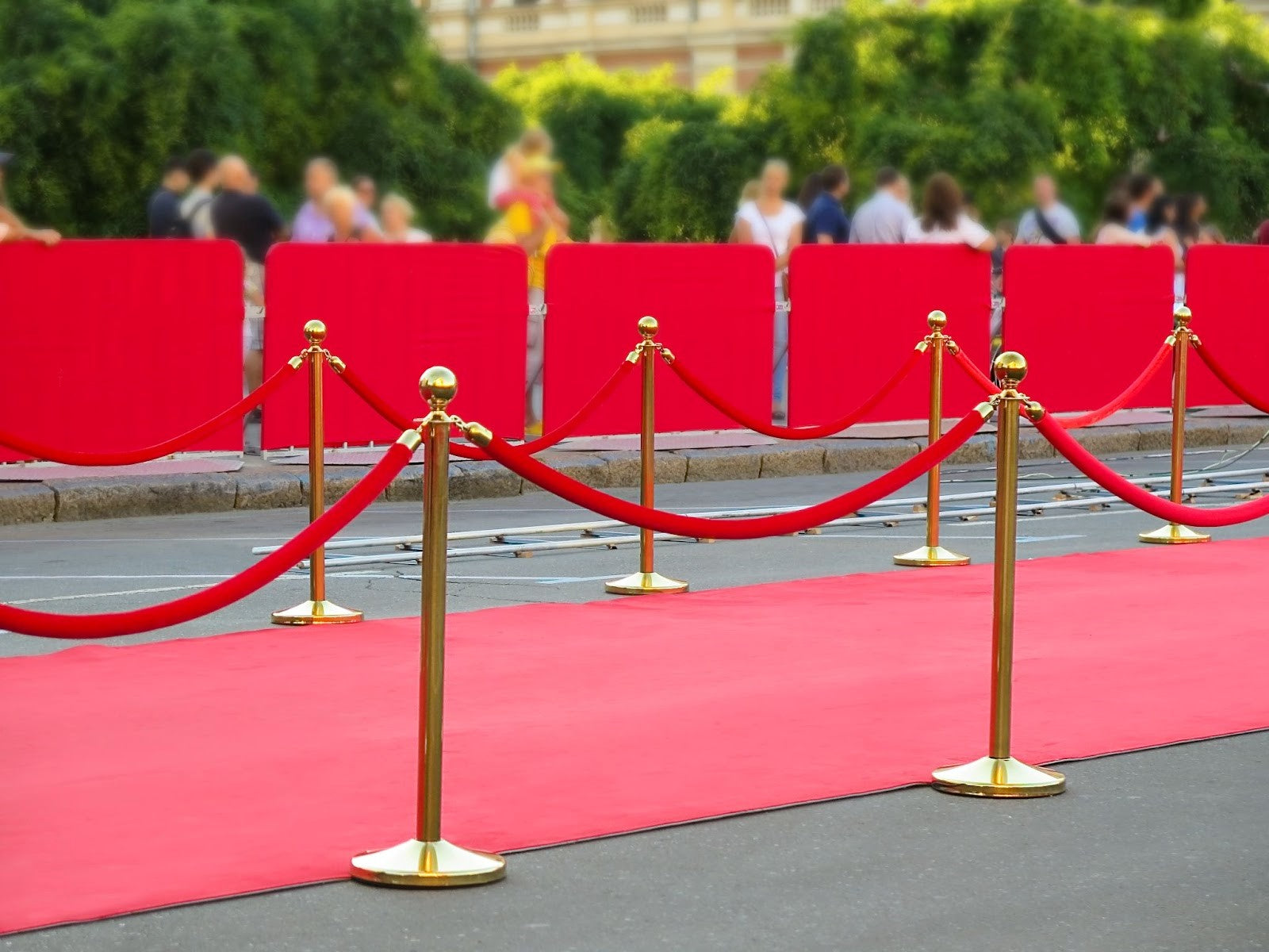 Red carpet runner set up outdoors in rope barrier with people watching