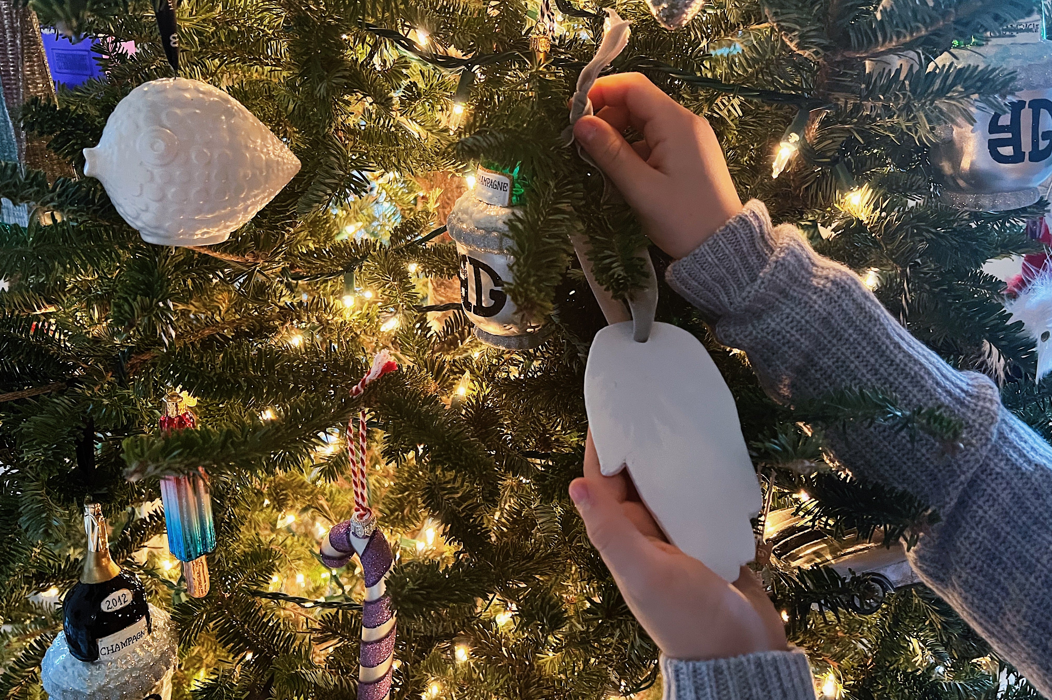 small hands hanging a custom clay hand ornament on a Christmas tree