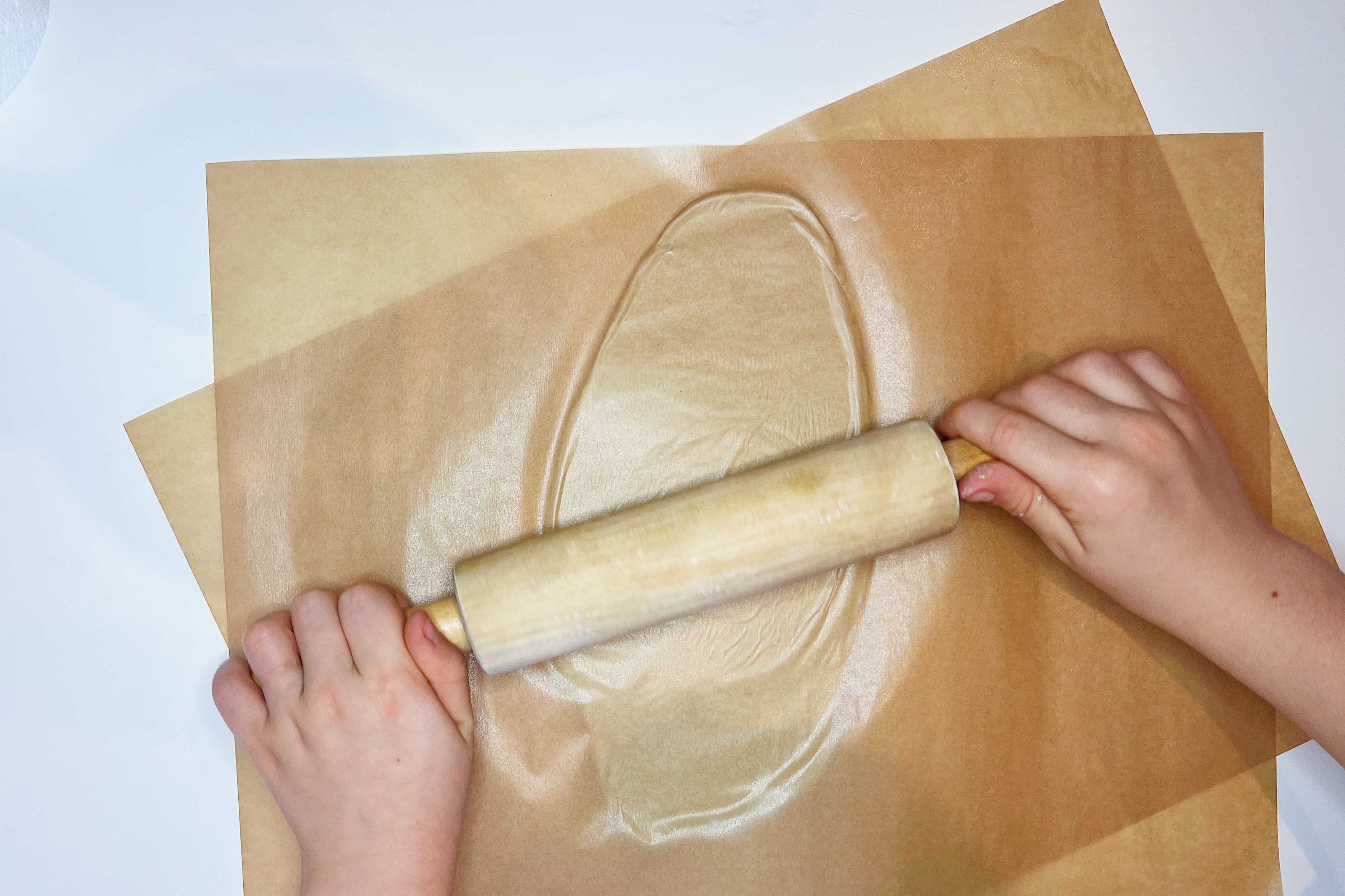 hands on a rolling paper rolling out clay between two sheets of parchment paper