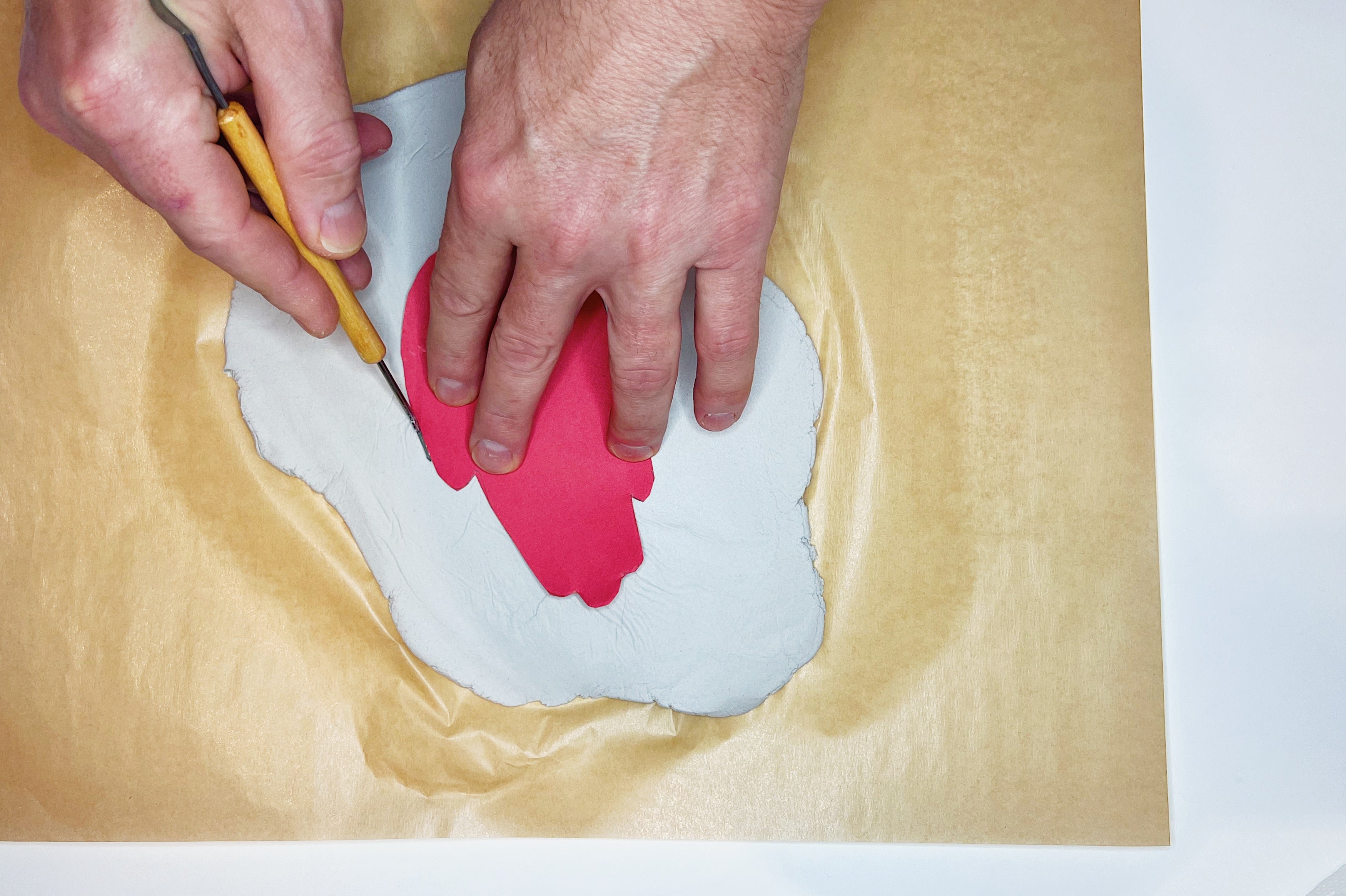 hands using a clay cutting tool to cut out the shape of the ornament from air-dry clay