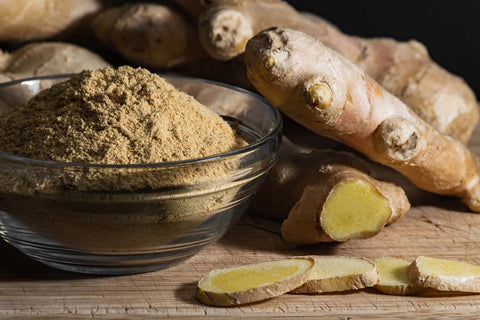 fresh ginger roots and sliced ginger pieces next to a bowl of ginger powder, highlighting the spice in both its natural and ground forms.