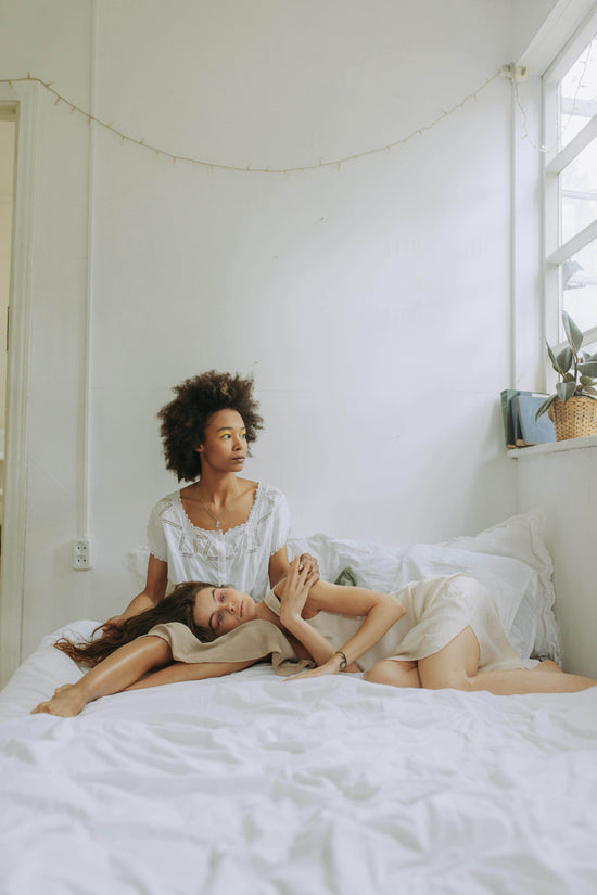 Zwei Frauen in weißen Kleidern liegen nebeneinander auf einem Bett.