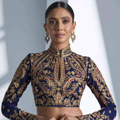 A woman wearing a high neck Paithani blouse with intricate gold embroidery, paired with statement earrings.