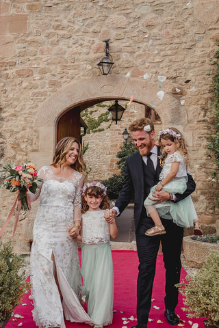 Photograph of the couple walking and smiling with two girls. Flower petals are in the air