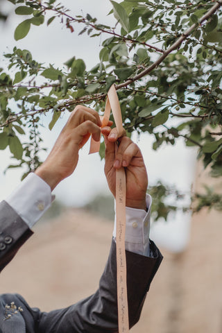 Photograph of the groom tying a ribbon on a branch of a tree during the ceremony