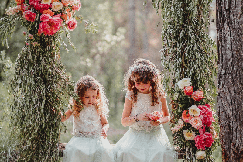 Photograph of Mireia's wedding, where two little girls are seen sitting, trees, and flowers