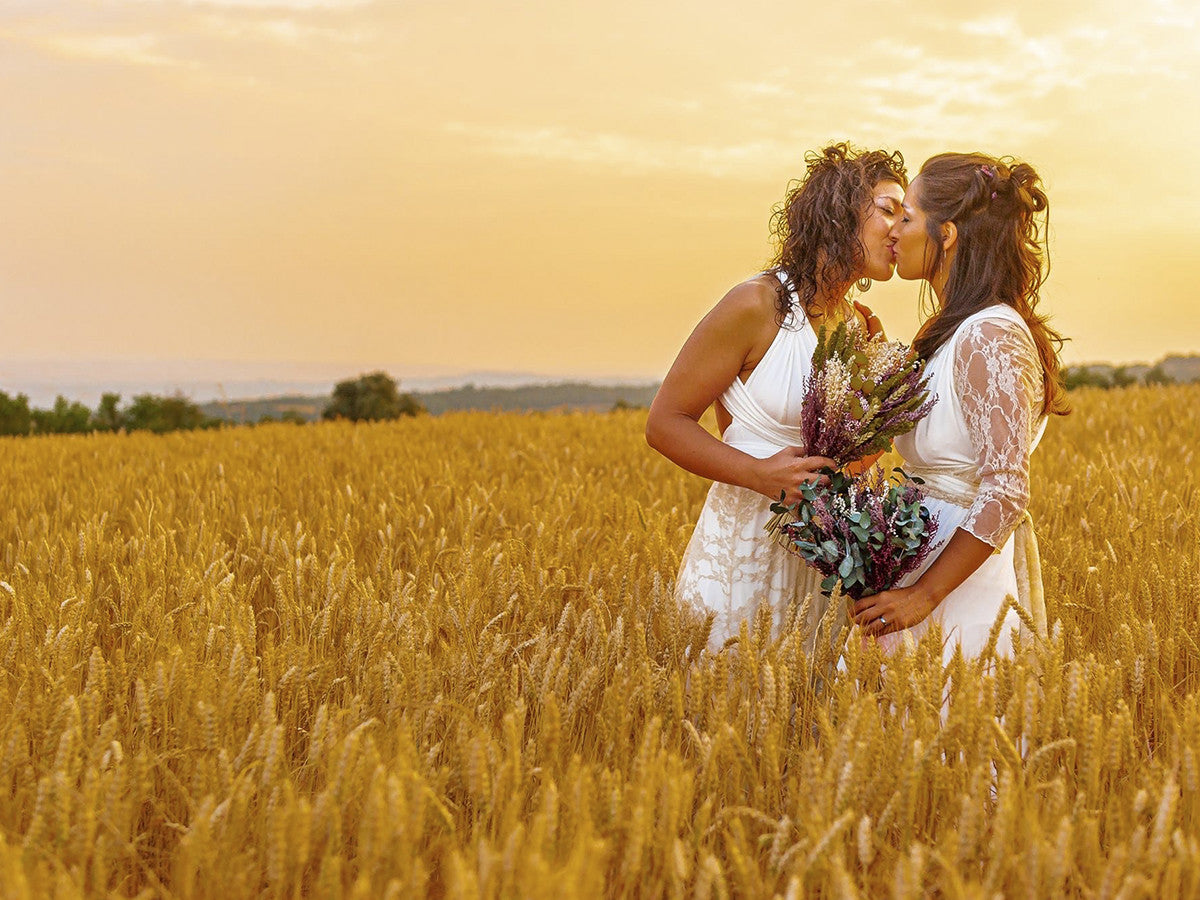 Two women in wedding dresses kissing in the field