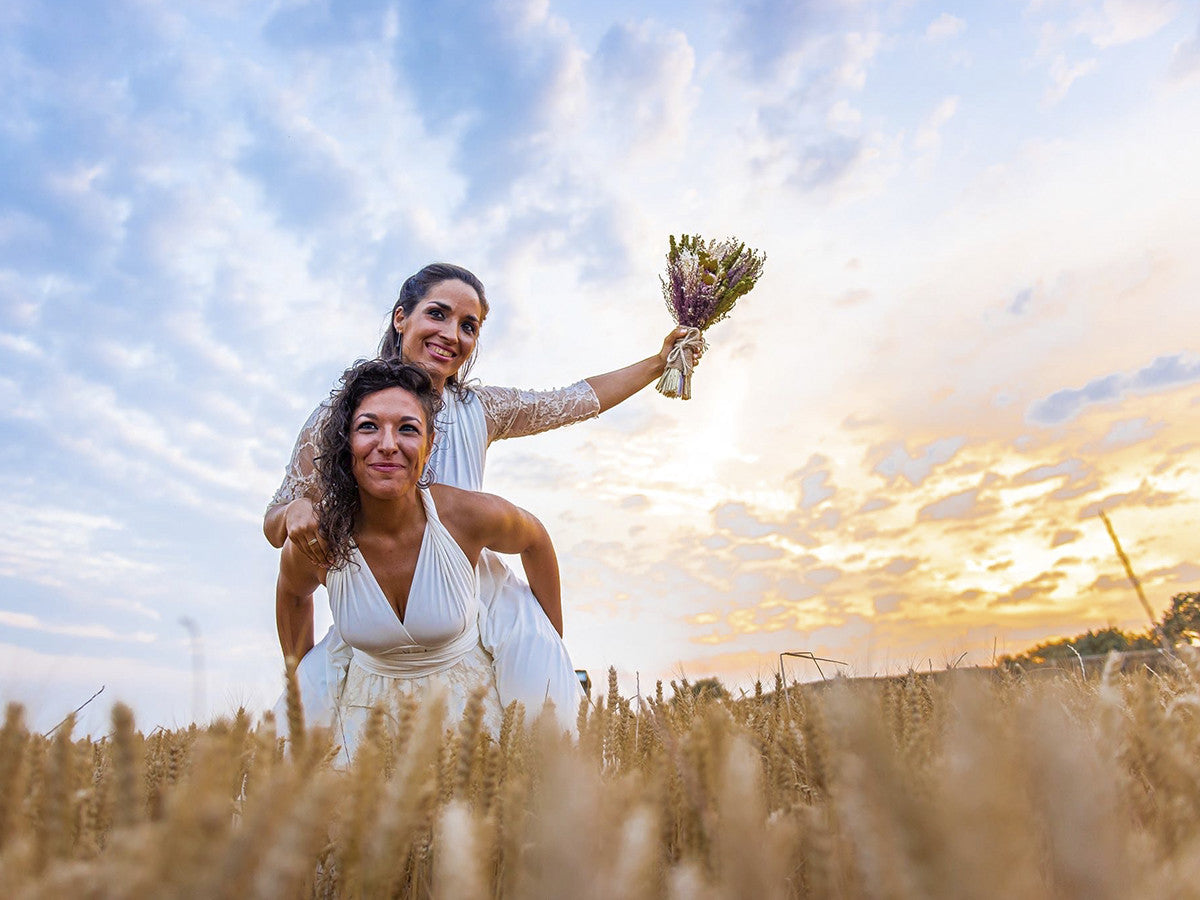 Dos mujeres el día de su boda gay, felices y sonriendo, una a caballito de la otra