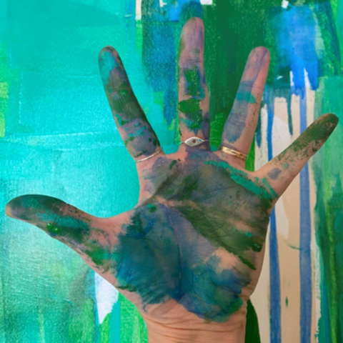 artist's hand covered in blue and green paint against a painting of blue and green paint