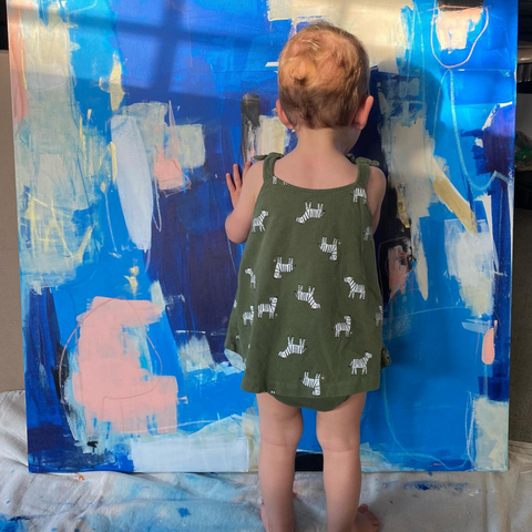 small child standing in front of a painting with blue and pink paint