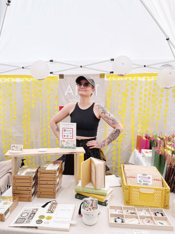 Image of Artist standing in booth behind her artwork for sale.