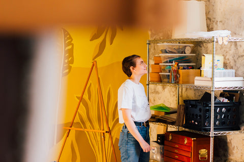 Image of Artist standing in yellow room next to shelves.