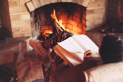 woman reading and reclining in a chair by the fire