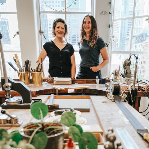 megan webb and jenna steele stand inside their melbourne studio with jewellery making tools and a plant in the foreground