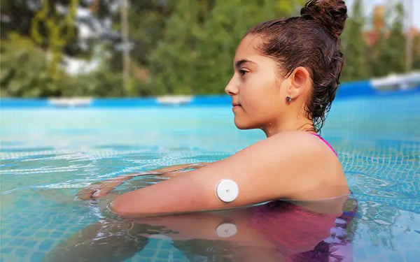 Flicka med diabetes typ 2 sitter i pool med en blodsockermätare på armen