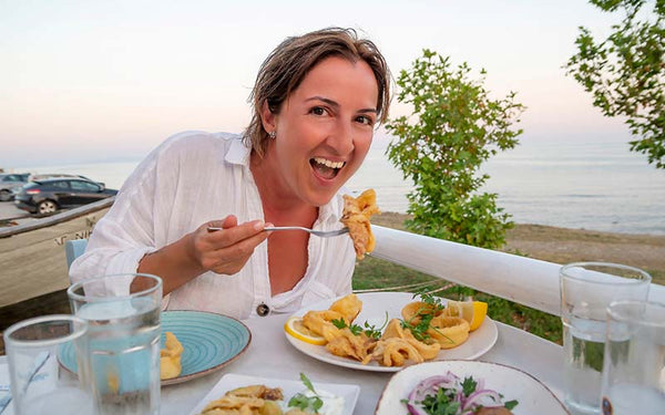 Kvinna äter medelhavskost (calamares) på stranden