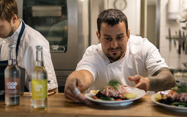 Kock på Skillinge Hamnkrog serverar räkmacka och två flaskor Good Idea bubbelvatten