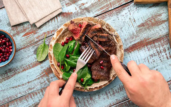 två händer vid ett bord, skär i kött och äter det proteinrika först.
