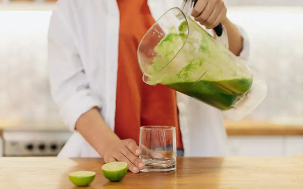 Kvinna häller upp en grön och nyttig smoothie i ett glas. Hon befinner sig i ett ljust kök