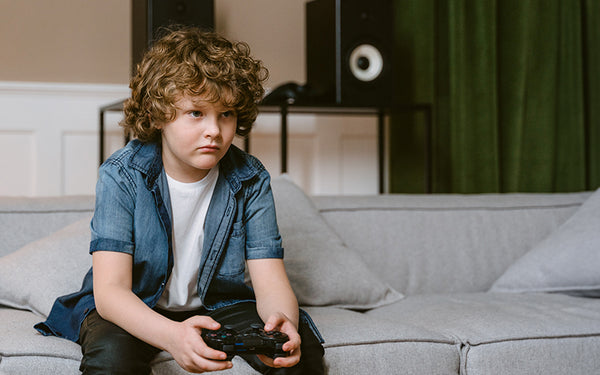 pojke med ohälsosamma vanor sitter hukad i soffa och spelar playstation