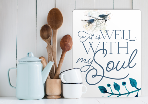 Sunshine Corner's Custom Religious and lake House sign that says "it is well with my soul" sitting on a white lake house kitchen counter besides a blue pot and wooden kitchen utensils.