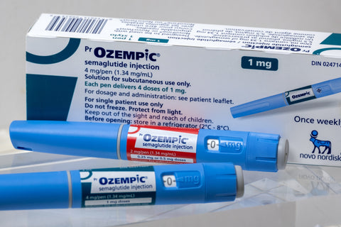 Two Ozempic injection pens lying in front upright Ozempic box with logo facing forward