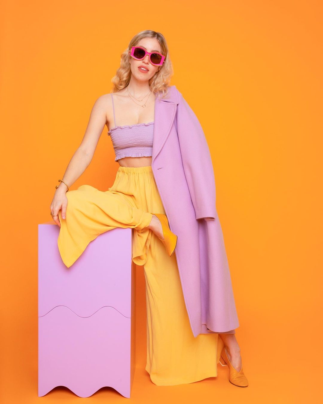 A woman standing with one leg leaning on the double sided wavy cube bundle from Moodelier with an orange background
