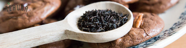 Black tea leaves in a wooden teaspoon next to chocolate cookies