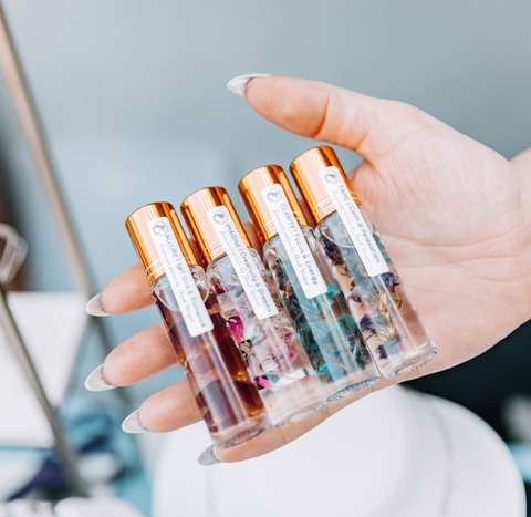 Beautiful glass bottles of fragrance or natural perfumes, filled with florals, crystals, and a clear liquid, each has a label with the intention and benefits