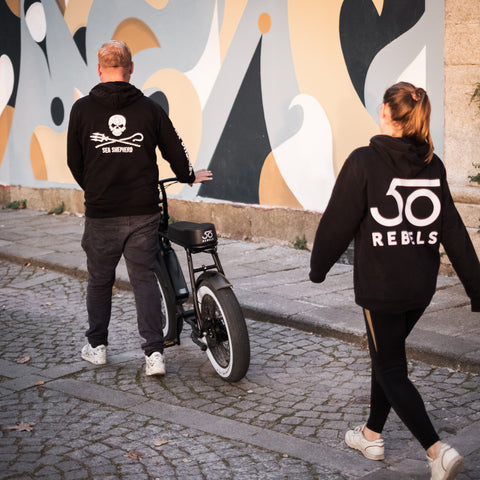 50 Rebels Founders walking the road on with a 50 Rebels e-bike and a hoodie with 50 Rebels logo on the back