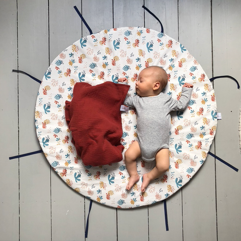 Bébé dort confortablement installé sur le tapis de jeu corail Carotte & Cie