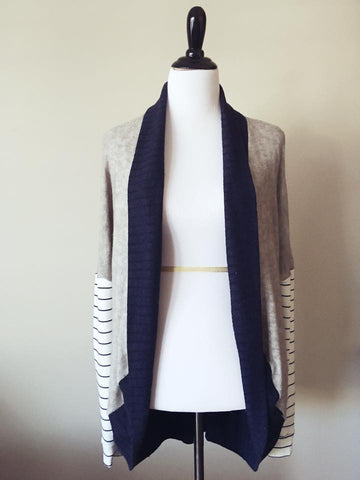 A cardigan sweater on a dress form with cream body and dark blue trim. 