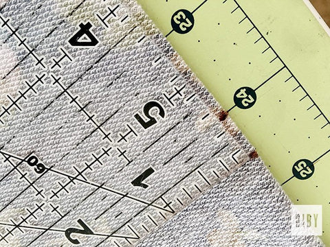 Clear ruler on fabric on a green cutting mat. 