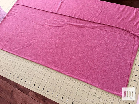 Pink knit fabric laid out on green cutting mat with markings for color bundle of tee shirt dress body.